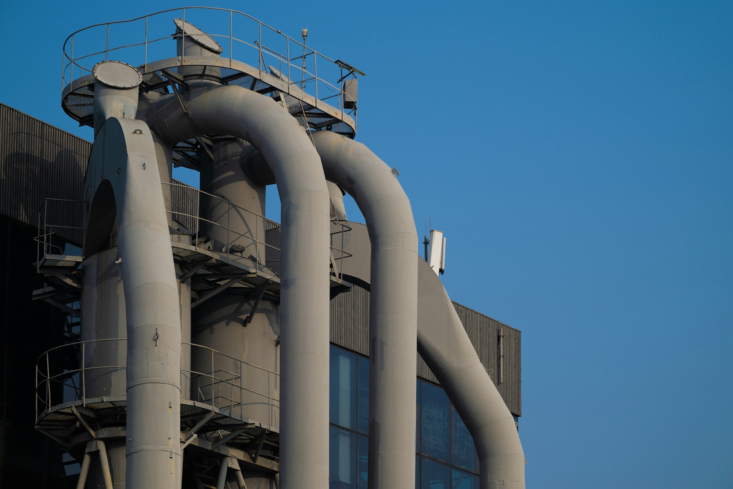 Grey process pipework rising against a clear blue sky